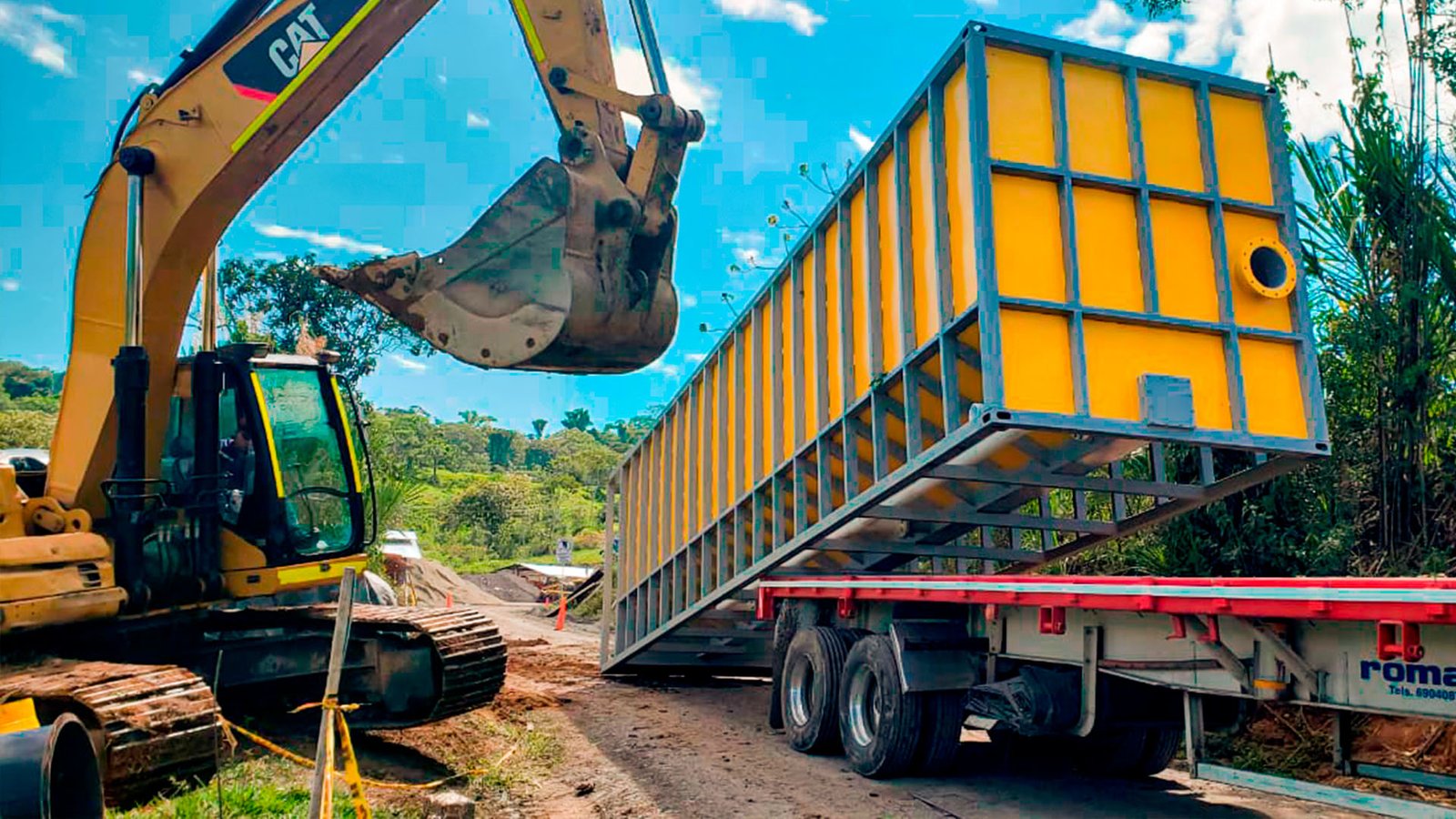 Camión rojo de plataforma larga transportando un gran decantador amarillo de la marca 'SYVERTECH' para el tratamiento de aguas residuales complejas, estacionado en una calle urbana con edificios y cielo despejado al fondo. - ver detalles